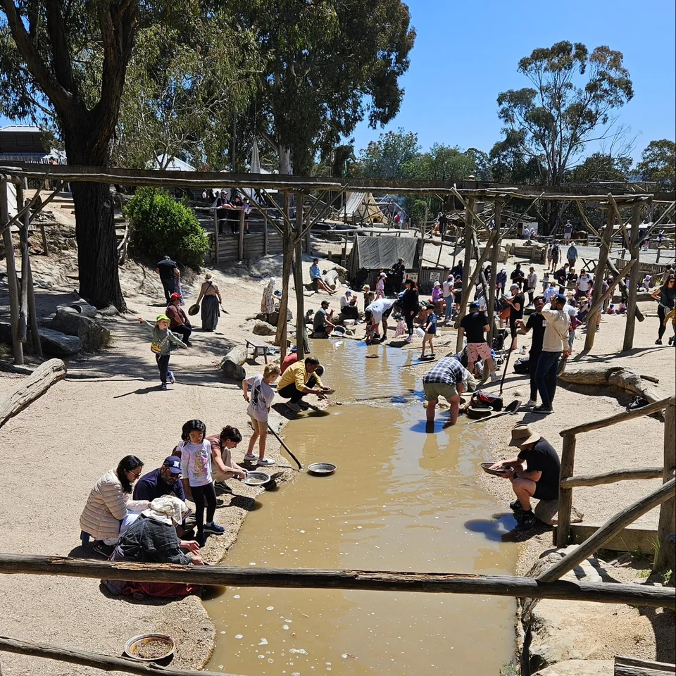 淘金小溪（The Diggings）熱鬧全景：木造導水槽旁大人小孩人手一隻金屬淘金盤，蹲在泥水裡洗出發財夢 · 11/03 11:32